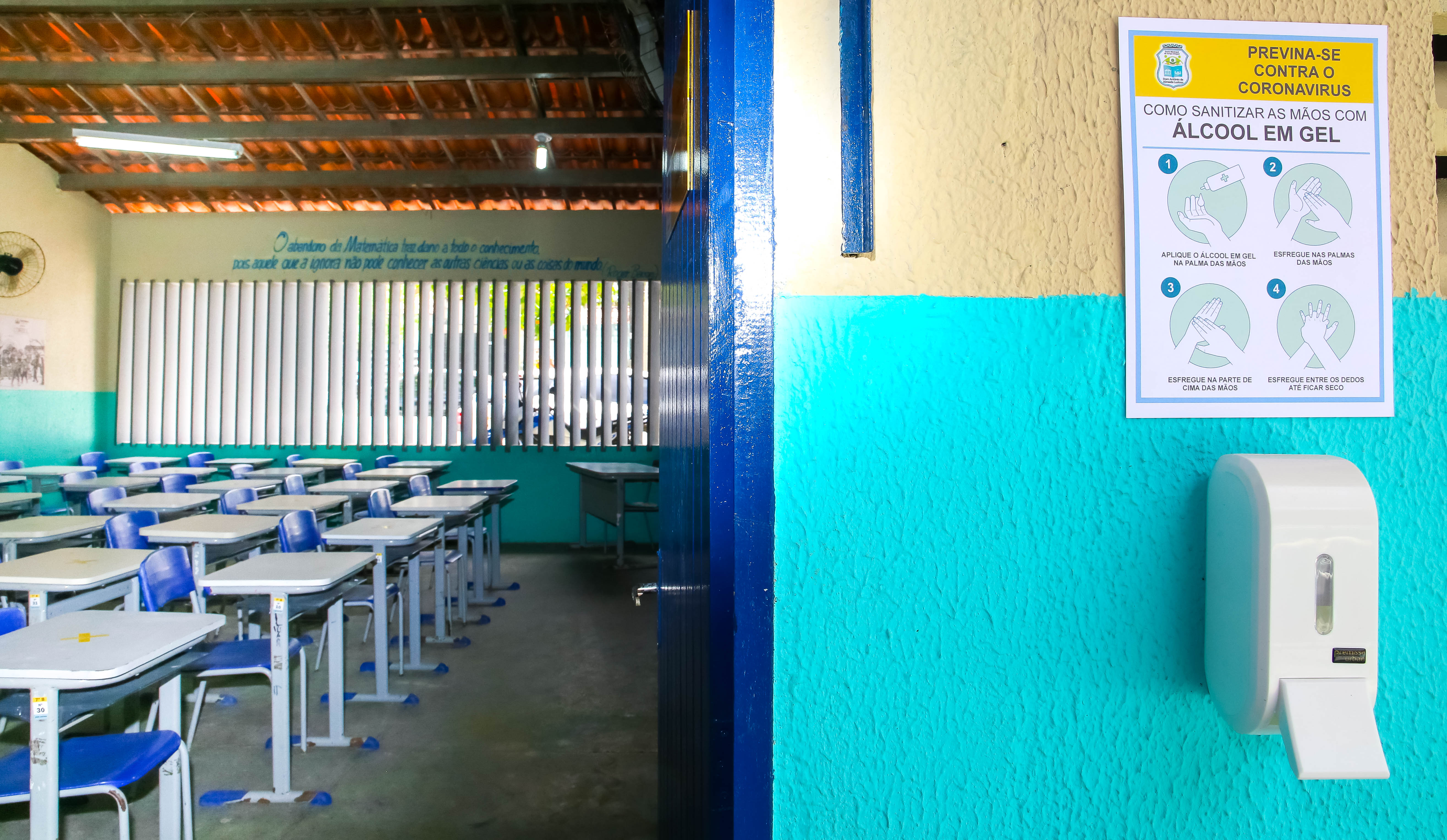 a foto mostra a porta de uma sala de aula aberta e, em segundo plano, as carteiras estudantis